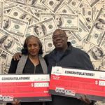 Michael and Rebecca Chesson stand in front of a money backdrop, while holding large, red Powerball checks.